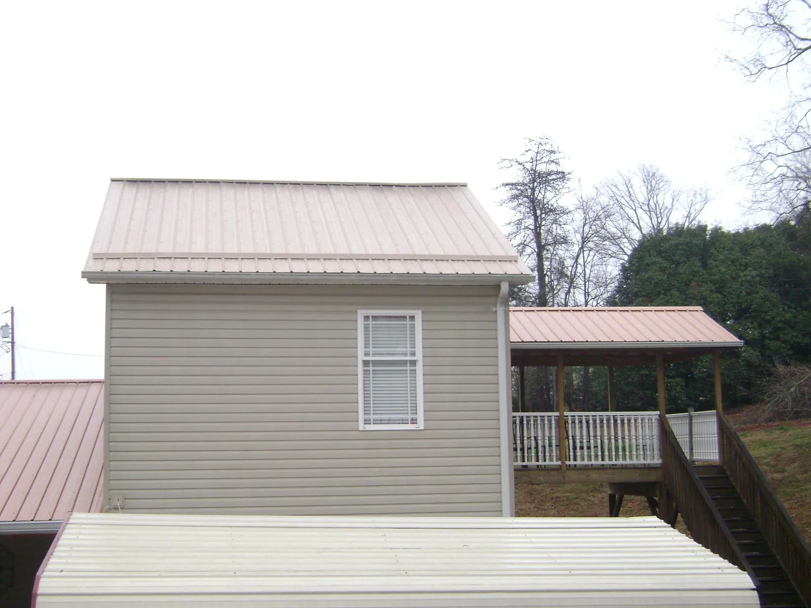 Tan metal roofs on a two story addition and attached porch, from a Roof Replacement job in Sparta